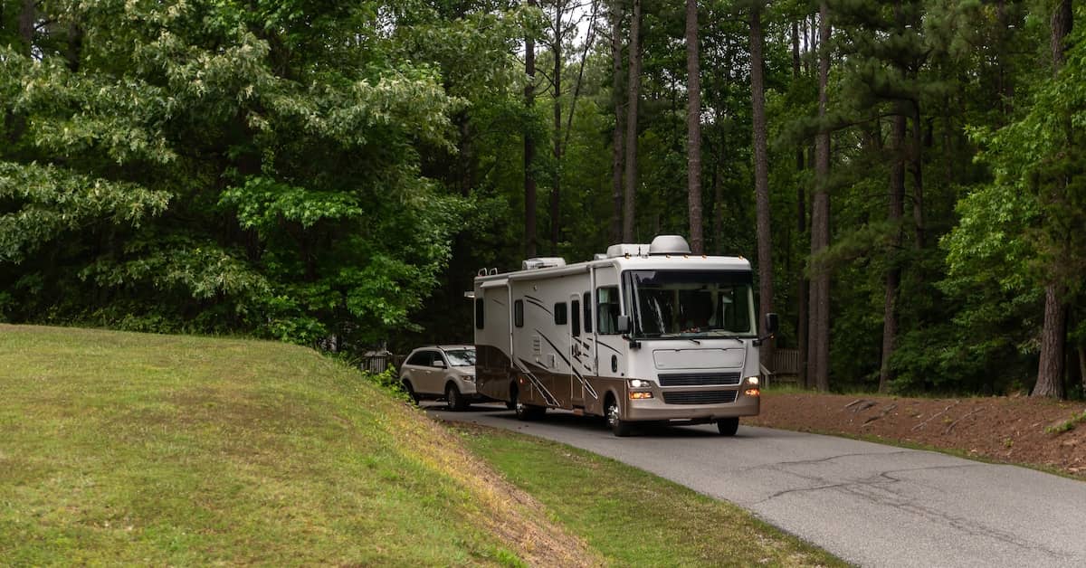 RV towing a vehicle to a campground in the woods | Fuller & Fuller